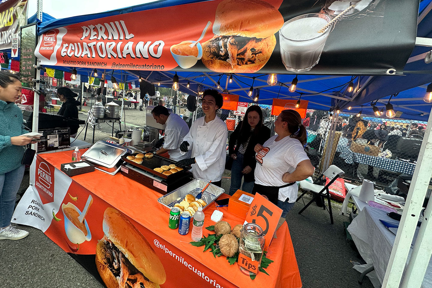 People cooking and serving food outside under a bright orange tent